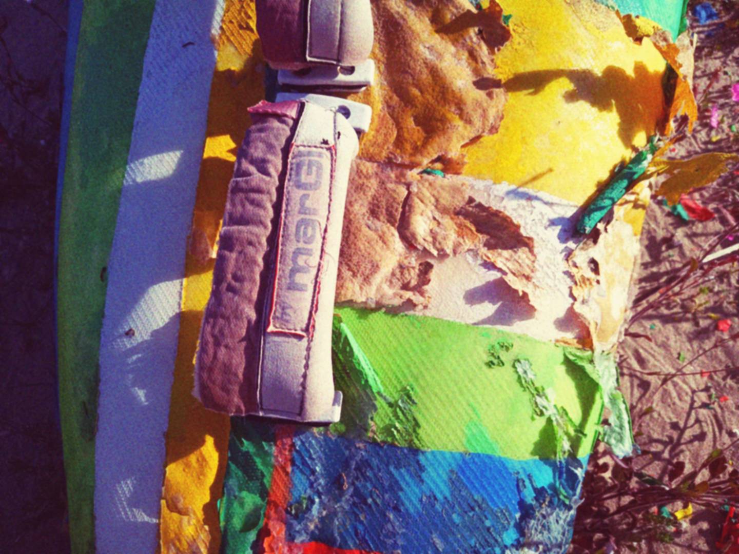 Tavola da surf molto colorata, ma in evidente stato di sfacelo, fotografata da vicino.